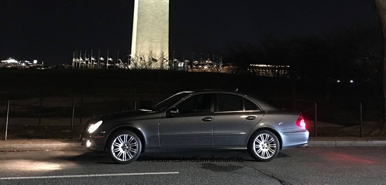 Bluish-grey color 4 door car parked near the Washington Monument. The picture taken at night. The car is a Mercedes-Benz.